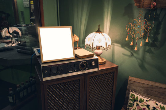 Antique audio player with blank frame and lamp shining on wood closet