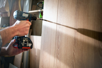 Craftsman drilling a hole by drill in a wooden board