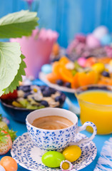 Easter breakfast. Fresh aromatic espresso coffee, orange juice, easter colored eggs, granola, on a blue background. Copy space