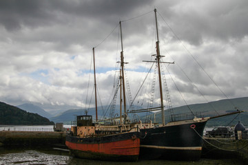 Fototapeta na wymiar two old sailing ships docked in the harbor under heavy clouds