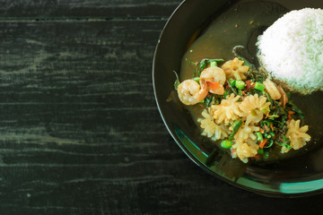 Spicy Stir-fried sea basil (squid, shrimp) with rice in a black dish on wood background. The traditional delicious food of Thai. Close up photo.