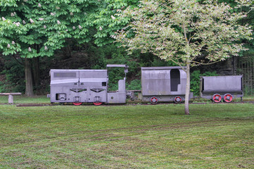  gray train with red wheels and wagons on the tracks in a park