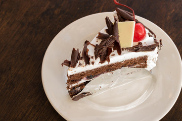 Chocolate cake with a red cherry fruit on top in a white dish, on a wooden table. It's a delicious popular menu. Close up photo.