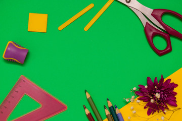 Back to school concept flat lay.Scissors,color pencils,sharpener,ruler,counting sticks and flower of chrysanthemum on the green and yellow background.Copy space for text,top view