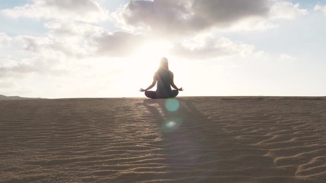 SLOW MOTION Gimbal moving in wide to close up shot of woman in yoga pose with crossed legs shot from behind. Relaxation and meditation in the desert. Summer sunset in desert.