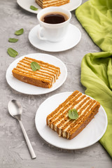 Homemade honey cake with milk cream and mint with cup of coffee on a gray concrete background. Side view, close up.