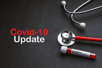 COVID 19 UPDATE text with stethoscope and blood sample vacuum tube on black background. Covid or...