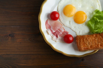 fried eggs, bacon and bread are on the plate on dark wooden background top view with emty space