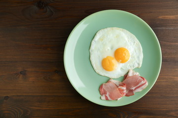 fried eggs and bacon are on the plate on dark wooden background top view with emty space