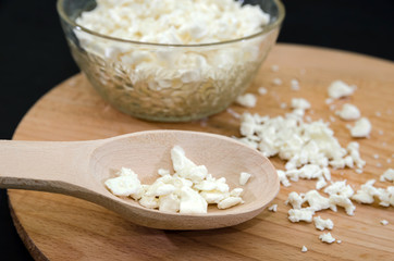 cottage cheese in a plate and a wooden spoon with cottage cheese on a wooden board. Black background. Close-up.