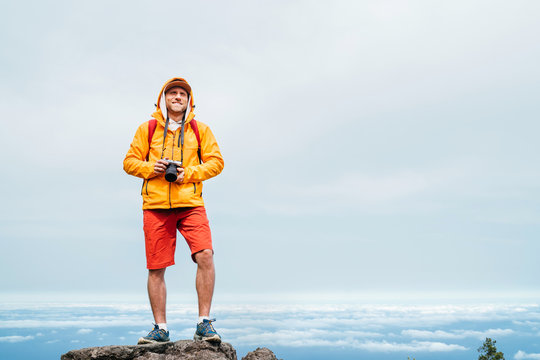 Young adult caucasian man dressed  sporty clothes with mirrorless camera on neck a enjoying view from Pico Ruivo mount 1861m - the highest peak on the Madeira Island,Portugal. Active vacation concept