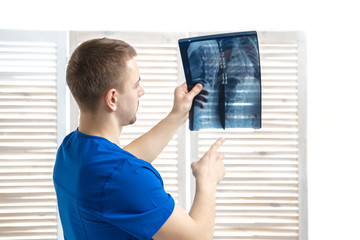 The doctor examines the x-ray image of the spine.The doctor is holding a photo of fluorography on a white background