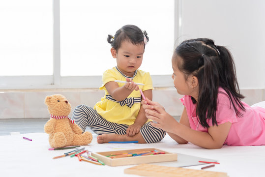 Little Asian girl playing with her younger sister, drawing together. Infant girl learns drawing with sister.