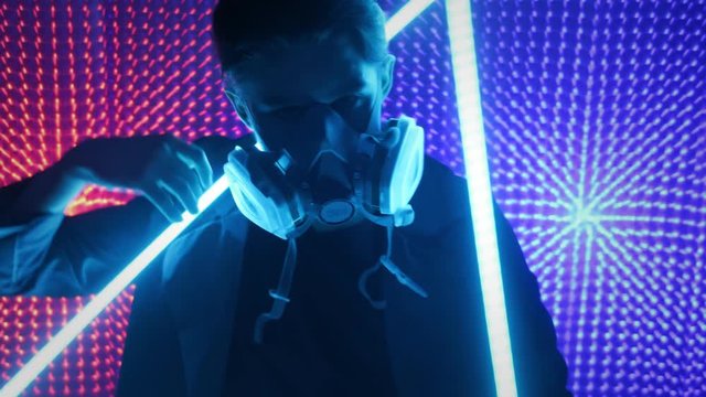 A model guy is dancing in a neon studio in a gas mask. Concept in dubstep style. Air pollution and global warming. Rave party.