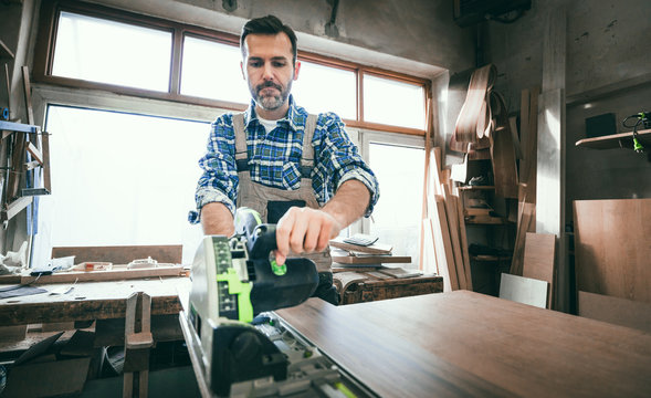 Carpenter using professional circular saw to cutting a wooden board in carpentry workshop