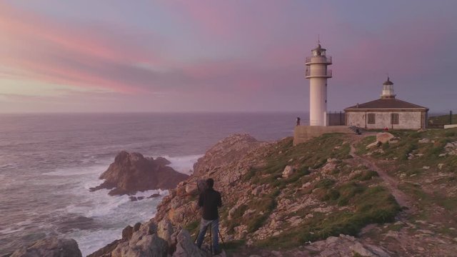 Photographer drone aerial view photographing a sea landscape view of Cape Tourinan Lighthouse at sunset with pink clouds, in Spain