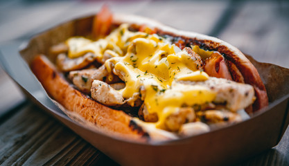 Philly cheese steak sandwich with meat, vegetables, cheese and sause in box on wooden table. street food