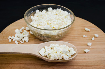 cottage cheese in a plate and a wooden spoon with cottage cheese on a wooden board. Black background.