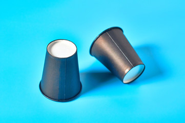 Two empty black cardboard glasses for hot beverages on blue background. Concept of environmental protection, coffee break, ecology, garbage recycle