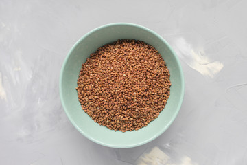 Raw buckwheat in ceramic bowl on gray background, concept of healthy eating vegan food. Close up, top view, selective focus, copy space