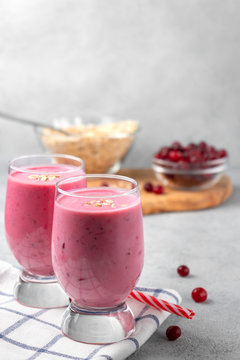 Two glasses with freshly homemade smoothie of yogurt, oatmeal and cranberries on a gray table. Healthy eating concept. Vertical image with copyspace