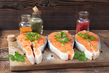 Three raw salmon steaks on a wooden cutting board prepared for cooking
