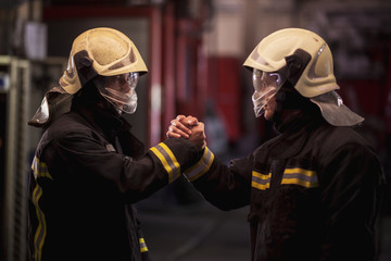 Two professional firemen congratulating each other. Firefighters wearing uniforms and protective...