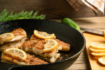 Portioned pieces of fried fish in a black cast-iron pan with fresh cucumbers and herbs. Traditional...
