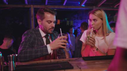 Attractive couple of businessman and young blondie talking on drinks at bar counter spending nice leisure time together on modern party.