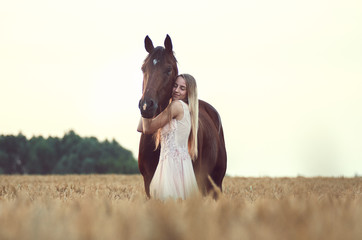 Mädchen umarmt ihr Pferd auf einem Weizenfeld in einem Kleid © Talitha