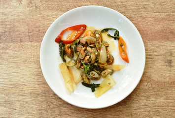 spicy stir fried mussel with slice onion and basil leaf on plate