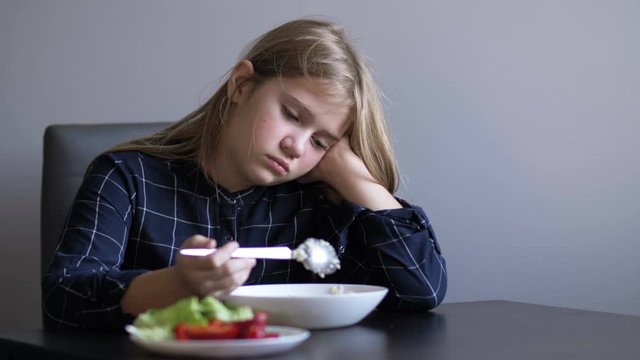 Little beautiful girl refuses to eat while sitting at the table in the kitchen. Children's whims