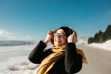 portrait of young European Muslim woman with hijab have fun at beautiful sunny winter day. Image of pretty woman walking in snowy mountains. She is wearing warm winter yellow scarf.