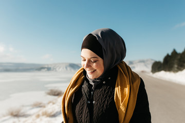 portrait of young European Muslim woman with hijab have fun at beautiful sunny winter day. Image of pretty woman walking in snowy mountains. She is wearing warm winter yellow scarf.