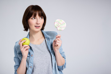 portrait of young woman or teenage girl with lollipop and green apple over gray background with copy space