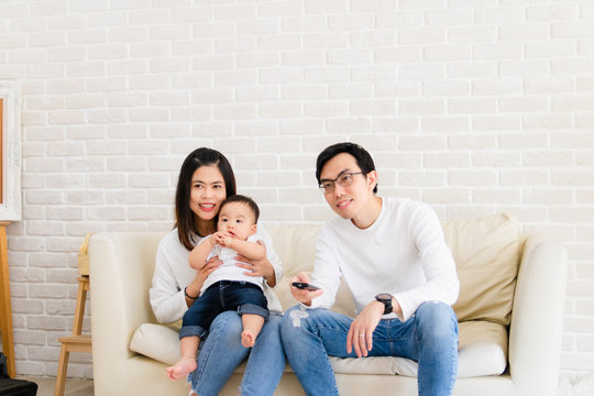 The concept of a happy family. Asian families consist of parents and baby sitting on the sofa watching TV happily. Family holiday