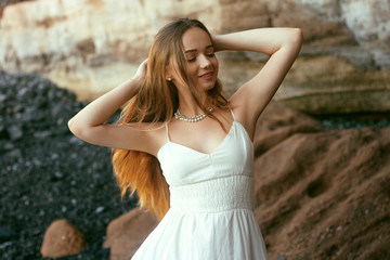 Fototapeta na wymiar Gorgeous girl in a long white dress on the ocean at the beach. The model is inherited by nature. Girl on vacation, light dress, summer, fashion. Gorgeous long hair develops in the wind. Tenerife