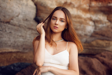 Fototapeta premium Gorgeous girl in a long white dress on the ocean at the beach. The model is inherited by nature. Girl on vacation, light dress, summer, fashion. Gorgeous long hair develops in the wind. Tenerife