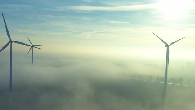 Camera flying along rotating wind wheels in backlit with ground fog(aerial view)