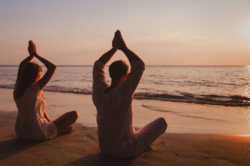yoga on the beach, couple silhouettes practice meditation and breathing exercises, lotus position