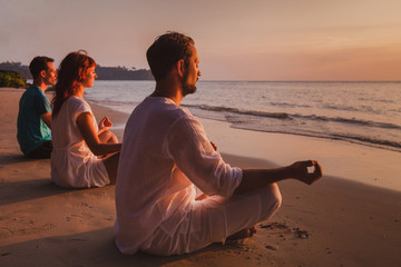 group meditation, people practicing yoga on the beach, relaxation and breathing excercises