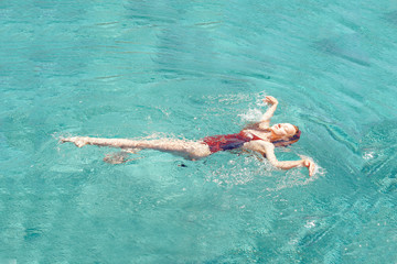 Happy girl swims in the pool. Top view of a girl in the pool, a stylish girl in a red swimsuit relaxes. Travel, rest, sun, summer.