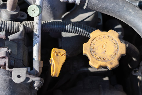 Oil probe and oil cap. Dusty details of a flat-four (boxer) car engine compartment under the open hood. Closeup view on a sunny day