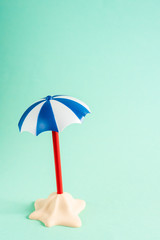 Little sand island with umbrella on pastel blue background. Minimal summer concept. Flat lay
