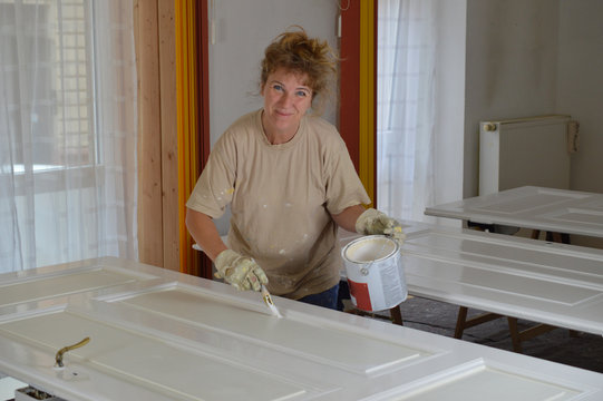 blond mature woman paining doors with white varnish as do it yourself