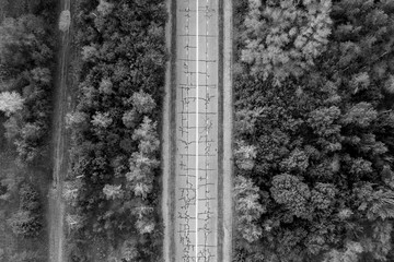 Aerial view of a of an empty abandoned road in the forest. Beautiful landscape with empty rural road. Top view from flying drone. Flat lay. Nature. Black and white photo