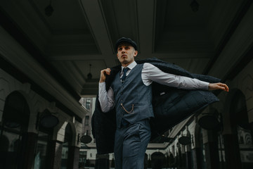 A man posing in the image of an English retro gangster in Peaky blinders style at city street.