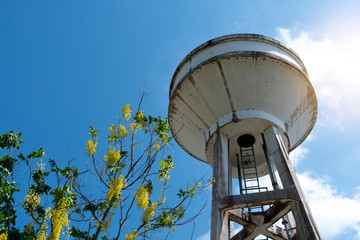 A water tank made of cement under the blue sky and has trees adorning the side.