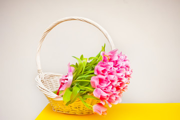 Pink tulips in a white basket on the yellow table
