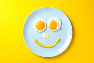 Smile face made of plate with fried eggs on yellow background, top view